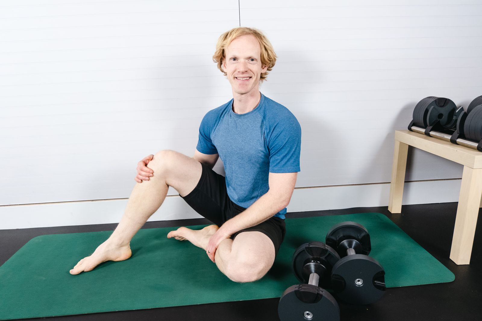 Kinesiologist Tim Begley seated on an exercise mat beside a set of dumbbells